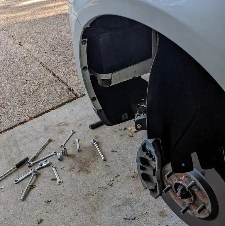 A close-up photo shows the front wheel well of a white car with the wheel removed, exposing the brake rotor and caliper. On…