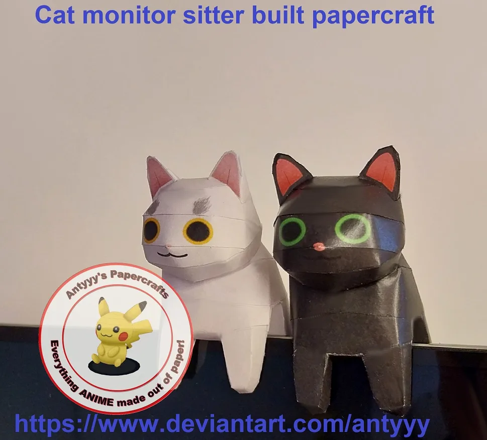 Two papercraft cat figures, one white and one black, sit side by side on a dark surface against a plain wall. The white cat…