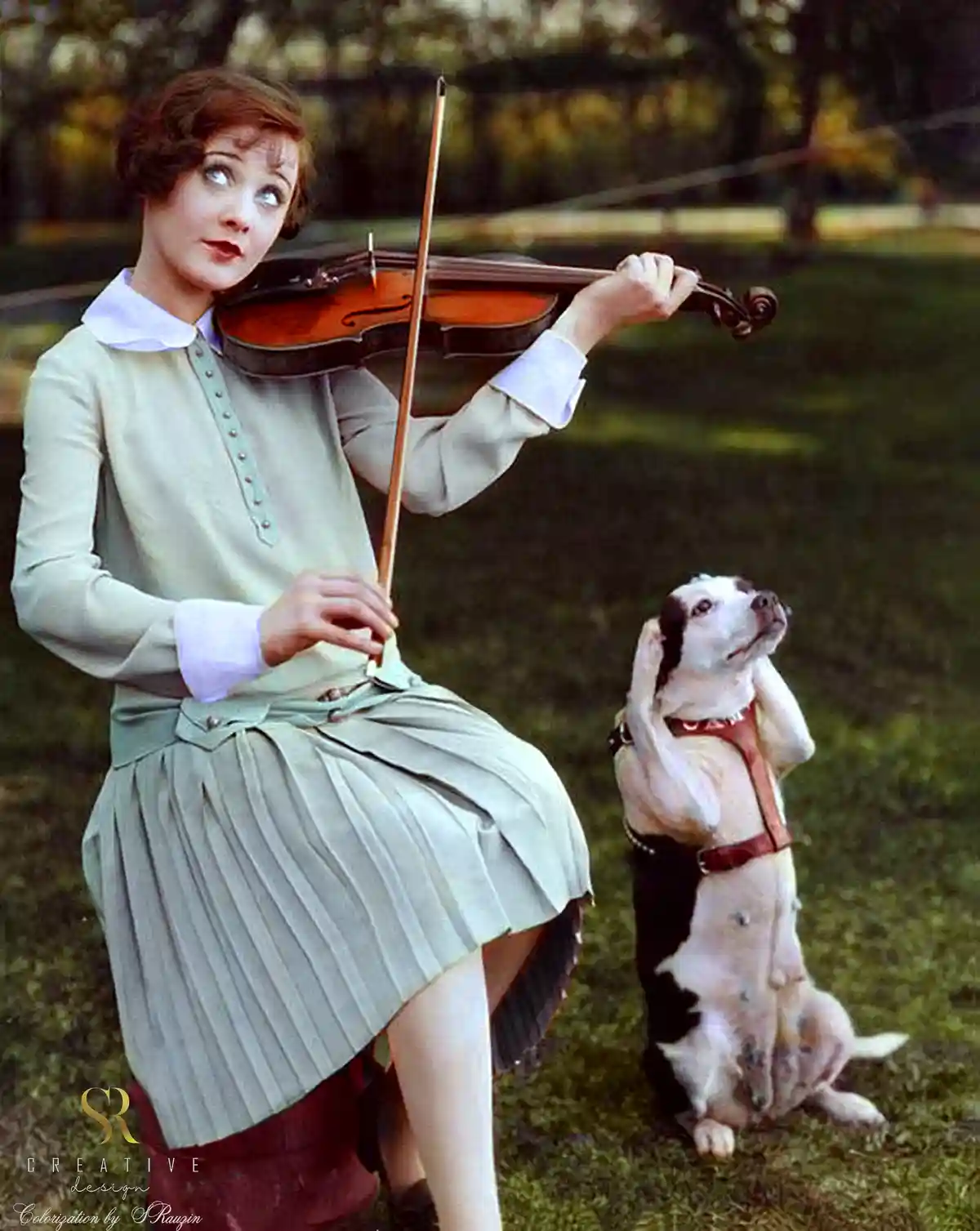 A vintage colorized photo shows a woman in a 1920s-style dress playing a violin outdoors, while a black-and-white dog beside…