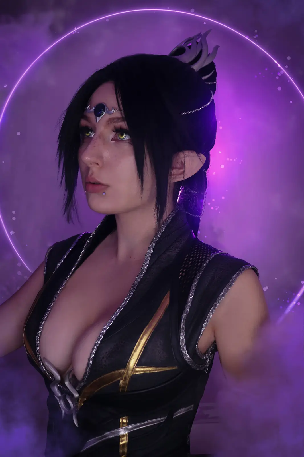 A person in cosplay as a fantasy character with black hair, pointed ears, and a dark outfit with silver and gold trim, set…