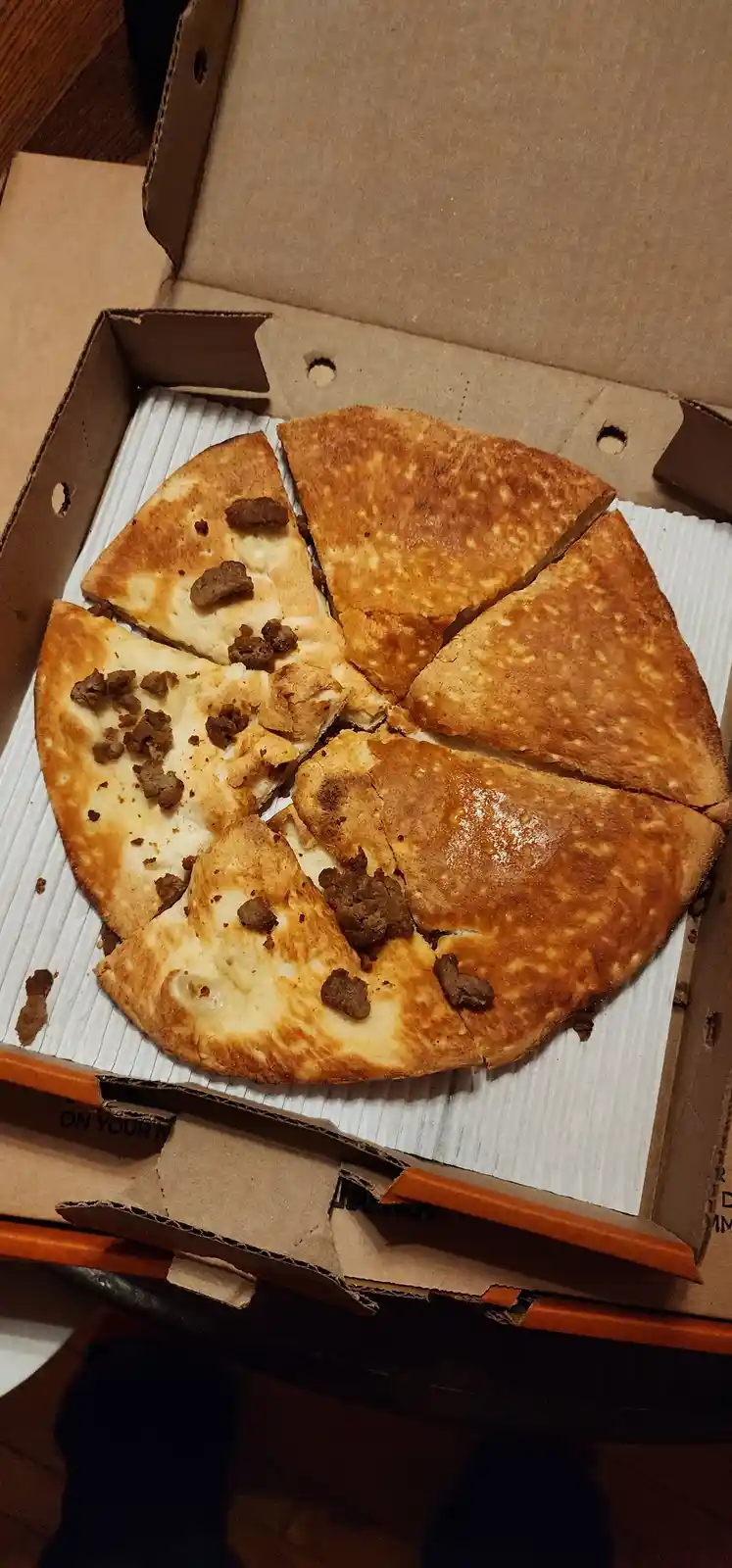 A pizza in a cardboard box is sliced into triangular pieces, but only half the pizza has toppings like cheese and meat…