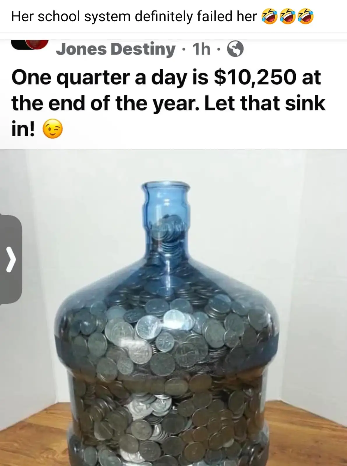 A large blue glass jug is filled to the brim with silver-colored coins, sitting on a wooden surface against a white wall…