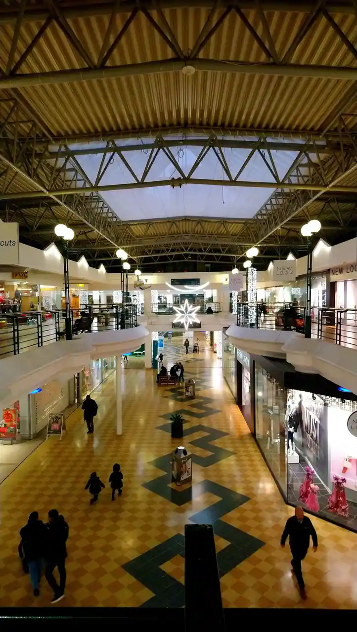 An overhead view of a multi-level shopping mall with a checkered floor, visible stores like 'New Look' and 'Duties', and…