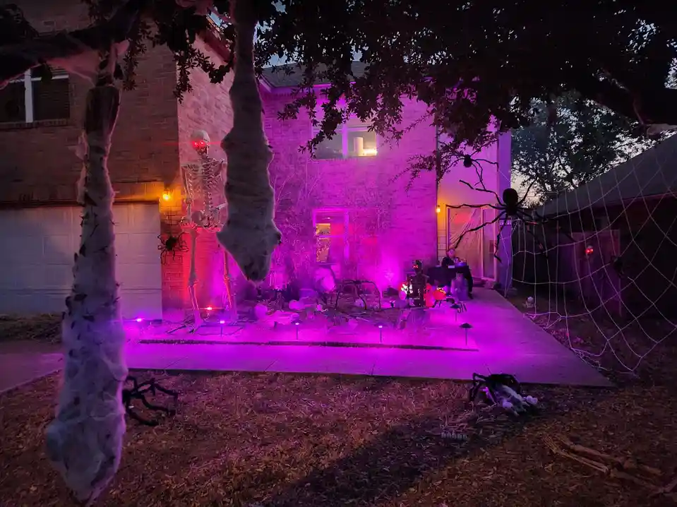 A house is heavily decorated for Halloween with glowing purple lights, a large skeleton with red glowing eyes, hanging…