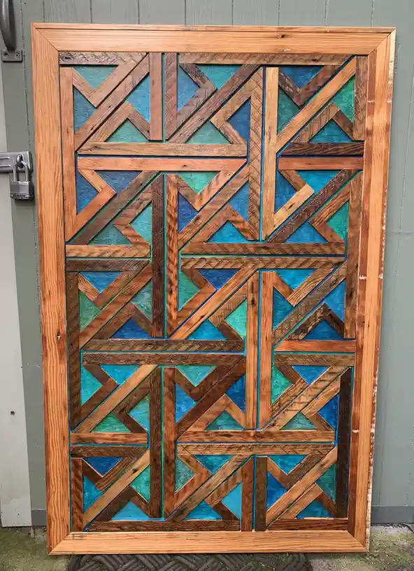 A large, ornate wooden door with a geometric pattern of interlocking triangles and rectangles, painted in shades of blue and…