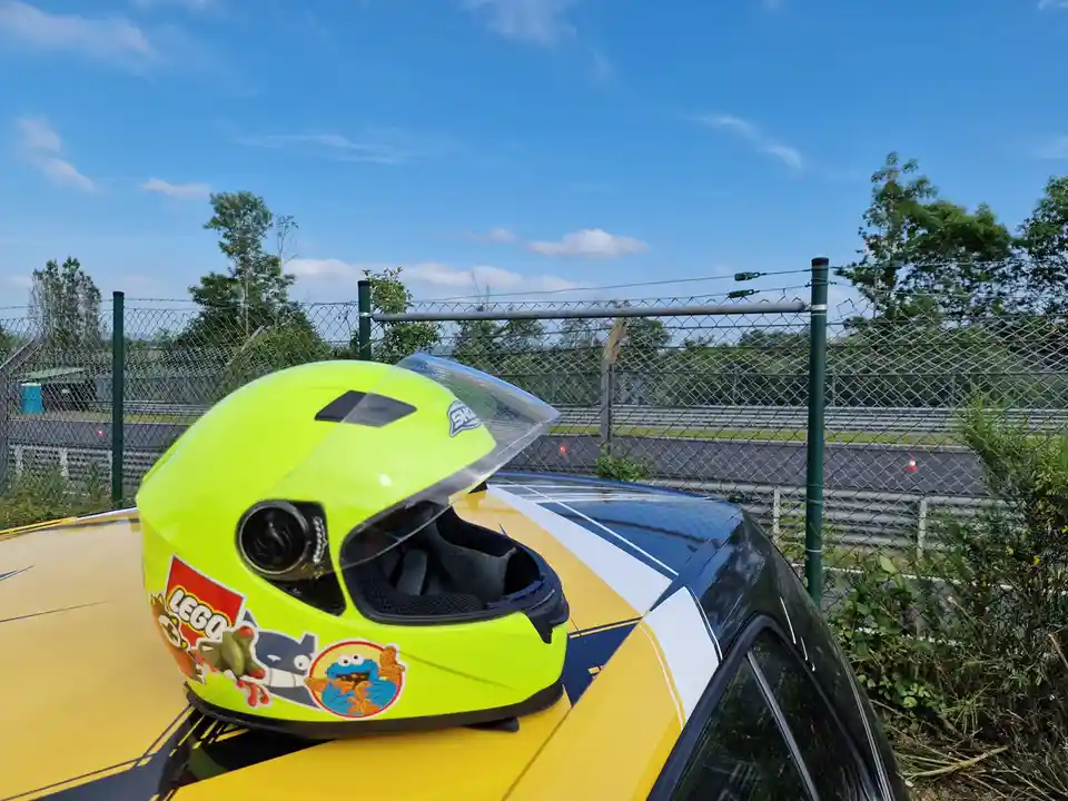 A bright neon yellow motorcycle helmet with stickers of LEGO and Cookie Monster sits on the hood of a yellow and black car…