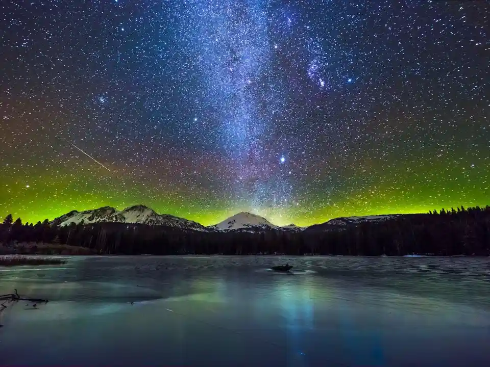 A breathtaking night sky photo shows a dense field of stars, the Milky Way, and a green aurora over snow-capped mountains…