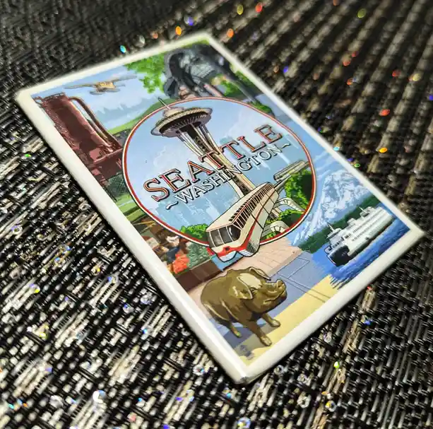 A rectangular souvenir magnet featuring a vintage-style illustration of Seattle, Washington, displays iconic landmarks…