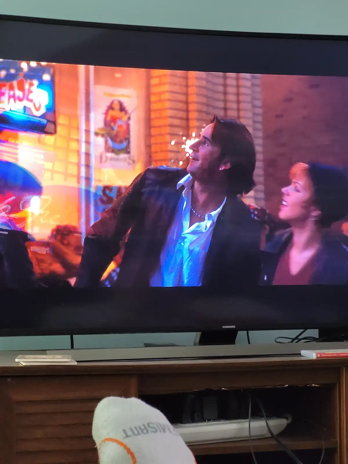 A television screen shows a scene from a movie or TV show featuring a man and a woman looking upward with sparkles visible…