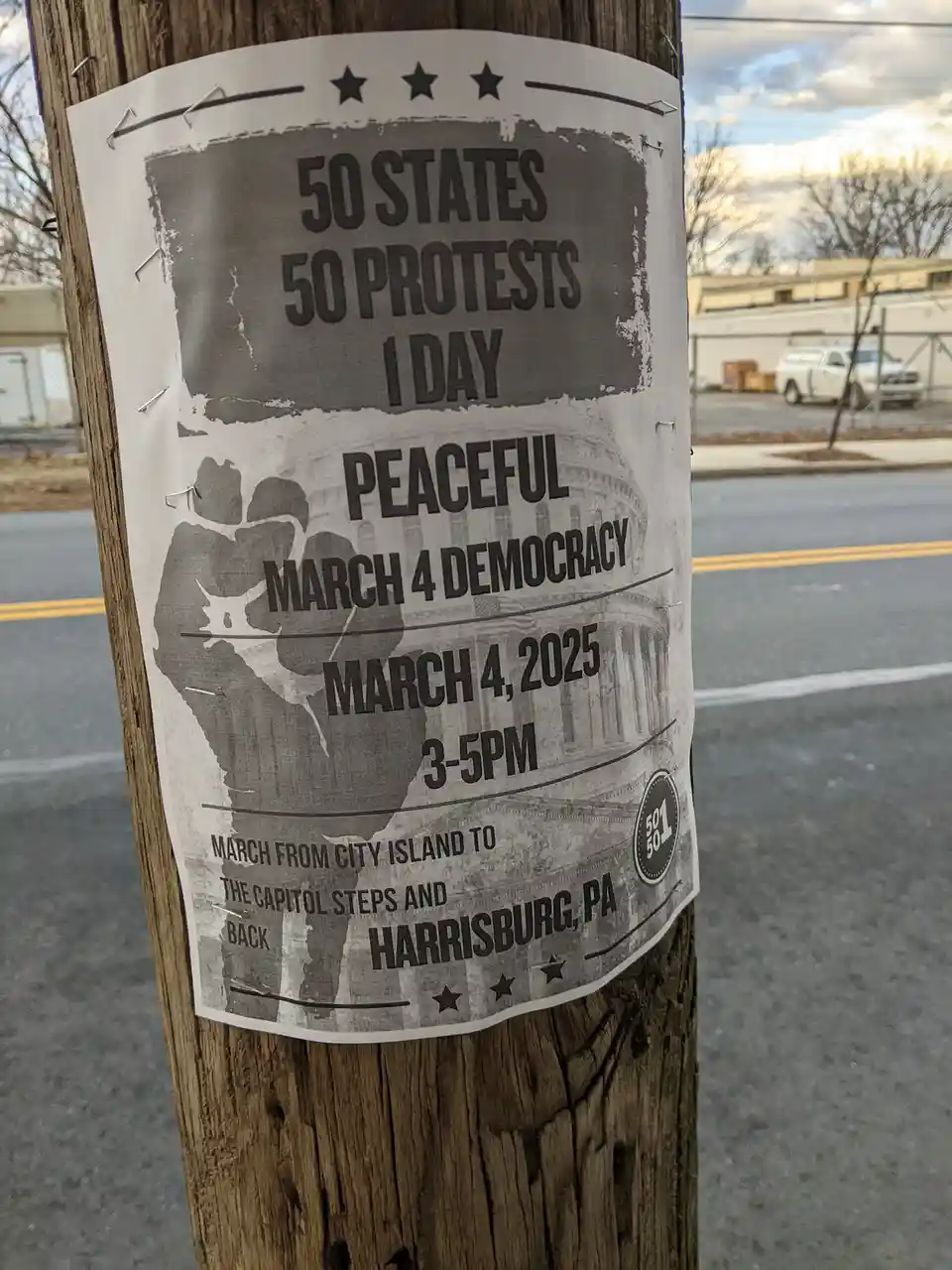 A black-and-white protest flyer is pinned to a wooden utility pole with staples. The flyer announces a 'Peaceful March 4…