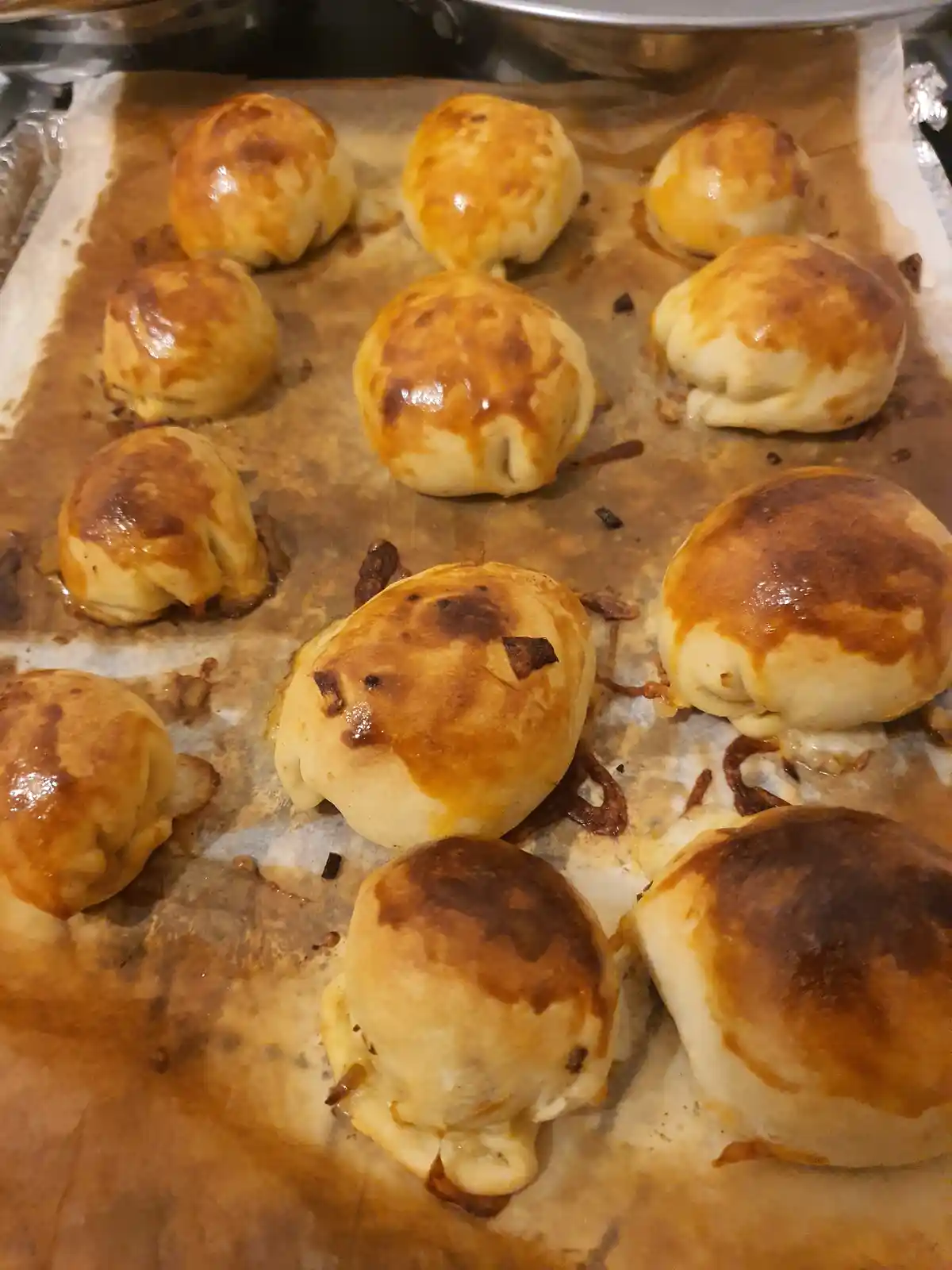 A baking sheet lined with parchment paper holds twelve golden-brown, round baked pastries with slightly burnt tops and…