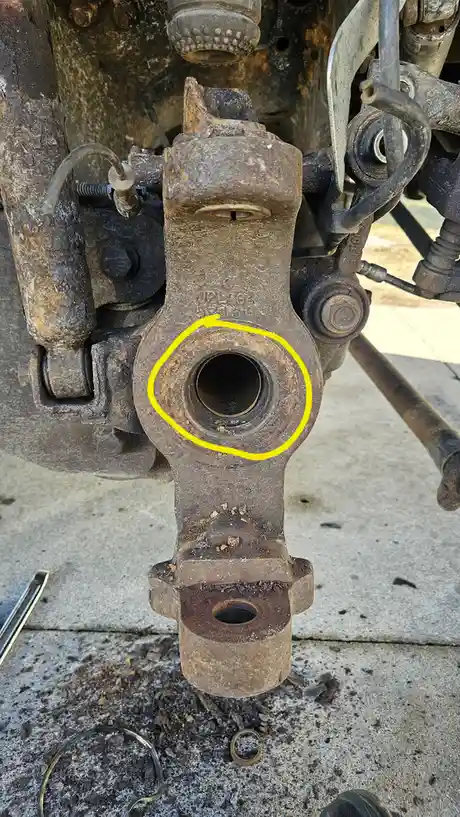 A close-up photo shows a rusty, dirty mechanical part, likely from a vehicle's suspension or steering system, with a…