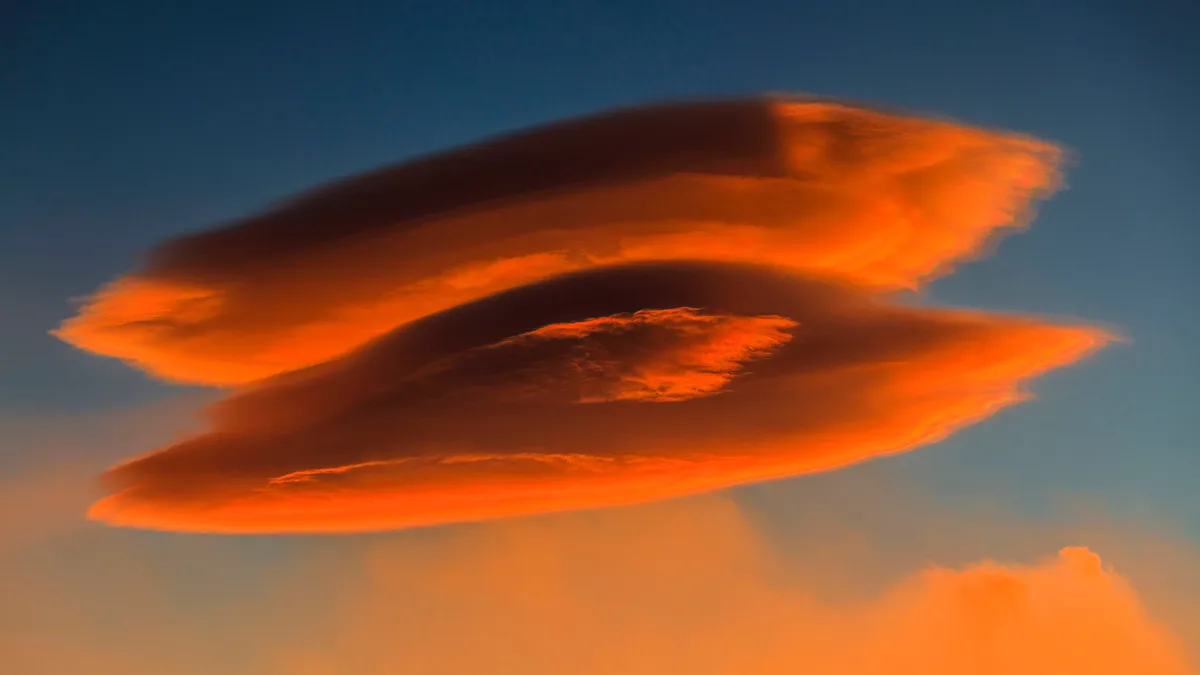 A lenticular cloud like a stacked pair of flying saucers sits motionless near Mount Etna's summit, against the backdrop of a…