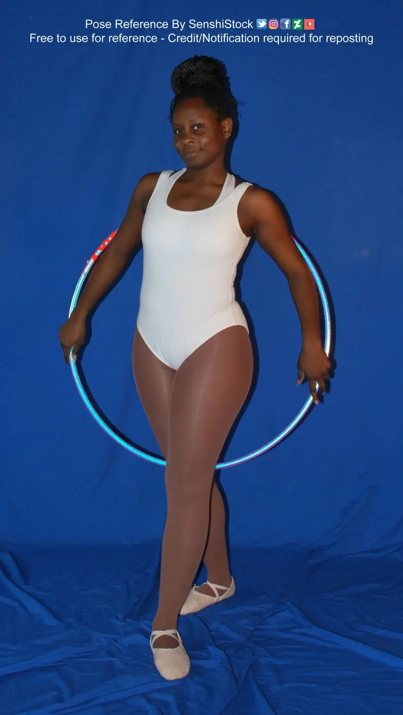 A woman in a white leotard and light brown tights stands against a blue backdrop, holding a glowing blue hula hoop around…