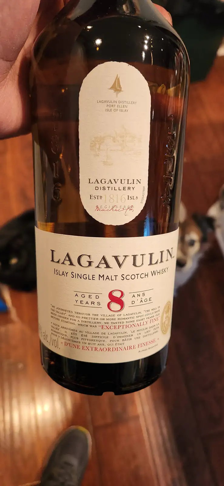 A close-up photo shows a hand holding a bottle of Lagavulin Islay Single Malt Scotch Whisky, aged 8 years. The label clearly…