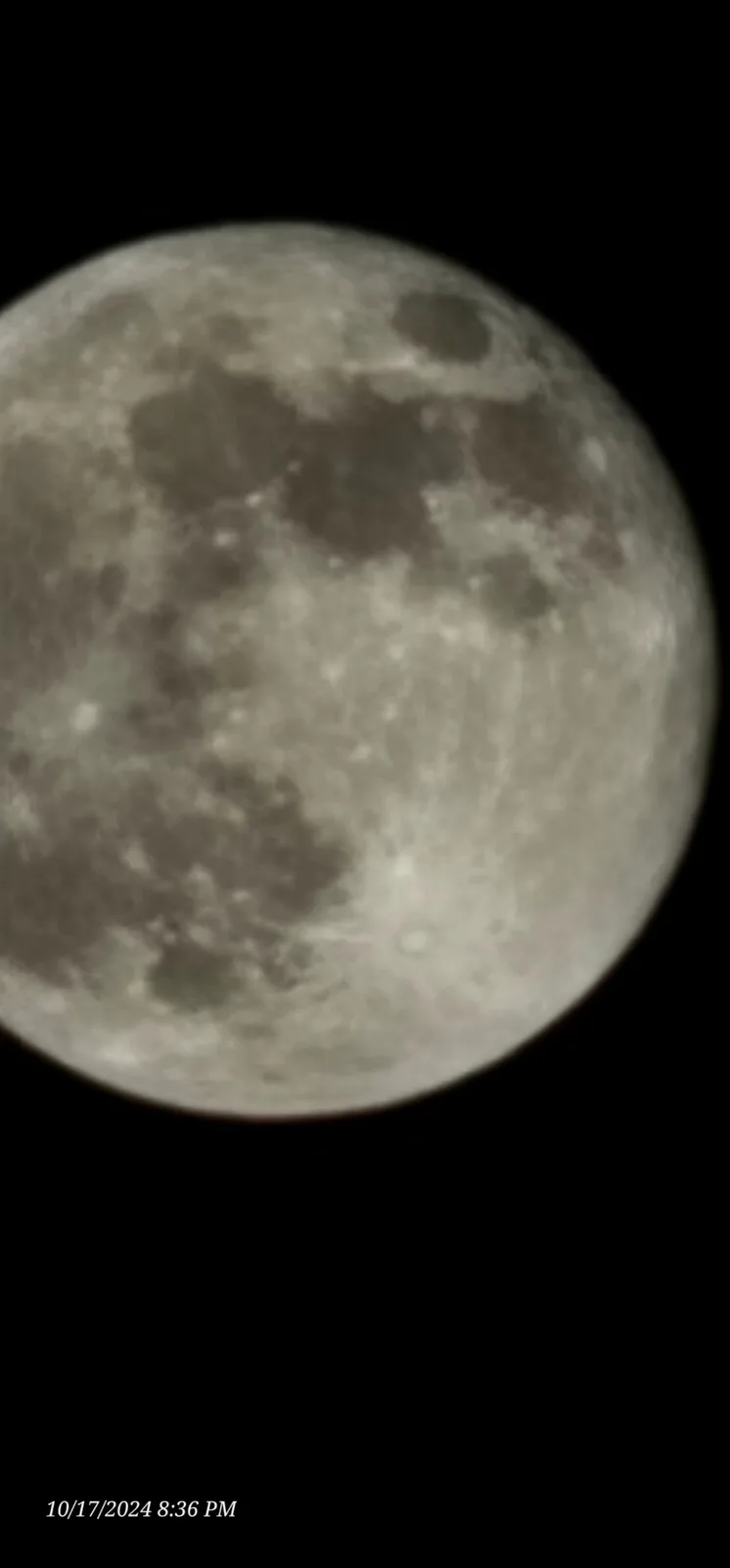 A close-up photograph of the moon against a black sky, showing its craters and surface texture, with a timestamp in the…