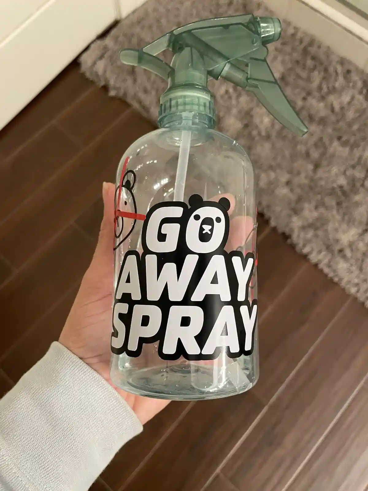 A hand holds a clear spray bottle with a green trigger nozzle, featuring bold white text with black outlines that reads 'GO…