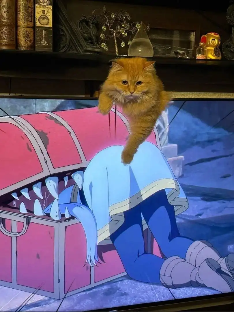 A fluffy orange cat is perched on the top of a television screen, appearing to be sitting on an anime character who is…