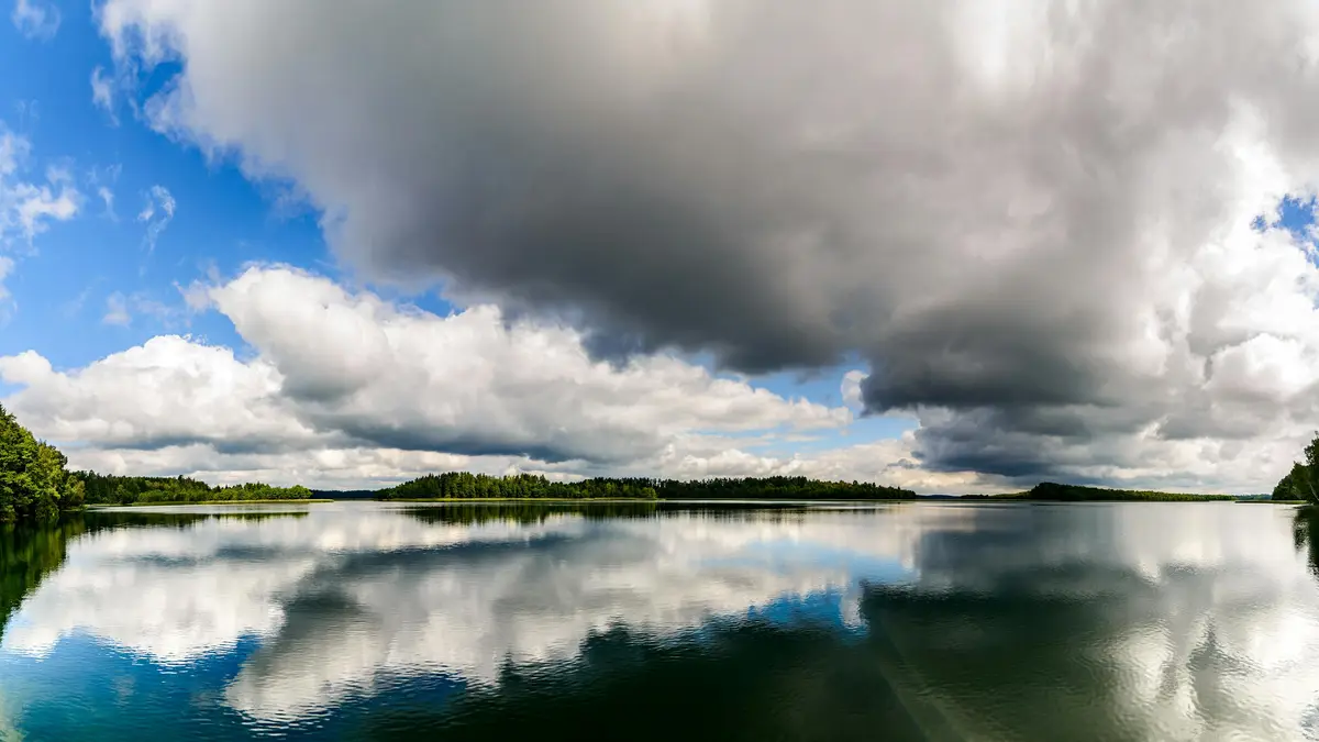 Towering cumulus clouds, a kaleidoscope of grays and whites, stretch across the sky, their ruffled peaks mirrored perfectly…