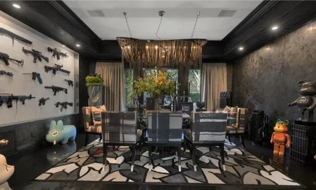 a luxurious dining room features a wall covered in numerous assault rifles mounted as decor, a large dining table with…