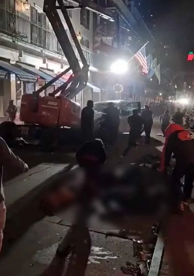A nighttime street scene shows a red construction vehicle and several people gathered around a blurred figure lying on the…