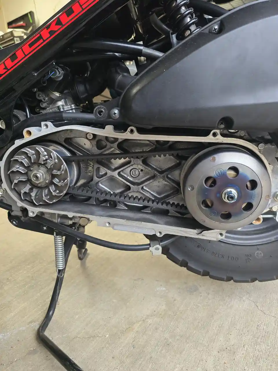 A close-up photo shows the exposed timing belt and pulleys of a motorcycle, with the engine cover removed, revealing the…