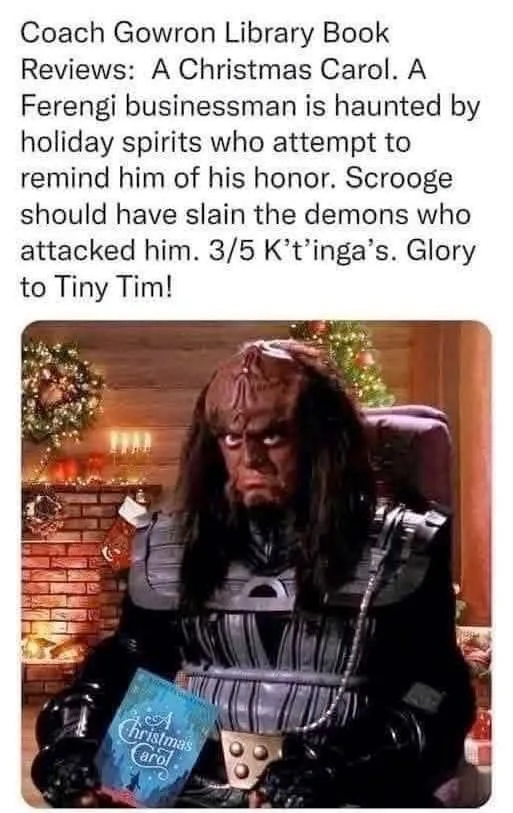A Ferengi character from Star Trek sits in a festive room holding a copy of 'A Christmas Carol,' with overlaid text…