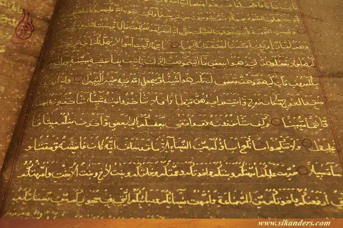 An open, aged manuscript with intricate Arabic calligraphy on a brownish parchment background. The text is written in…