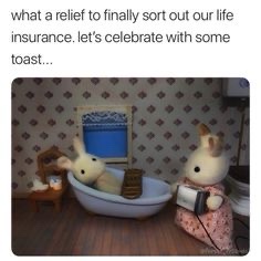 Two anthropomorphic rabbit dolls sit in a bathroom. One is in a bathtub holding a bottle, the other sits on the toilet…