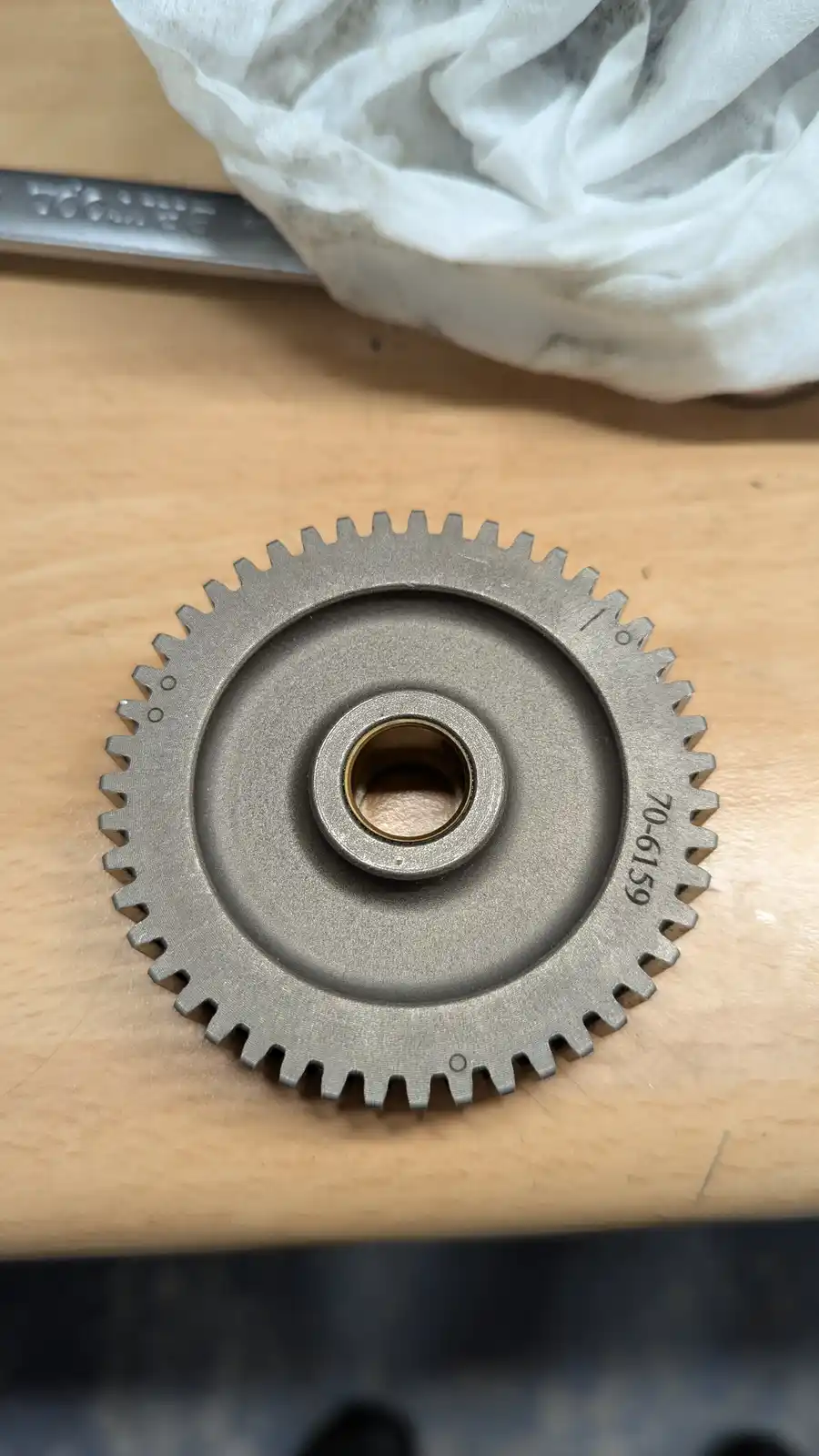 A close-up photo shows a metallic gear with the number '70-6159' stamped on its side, resting on a wooden surface next to a…
