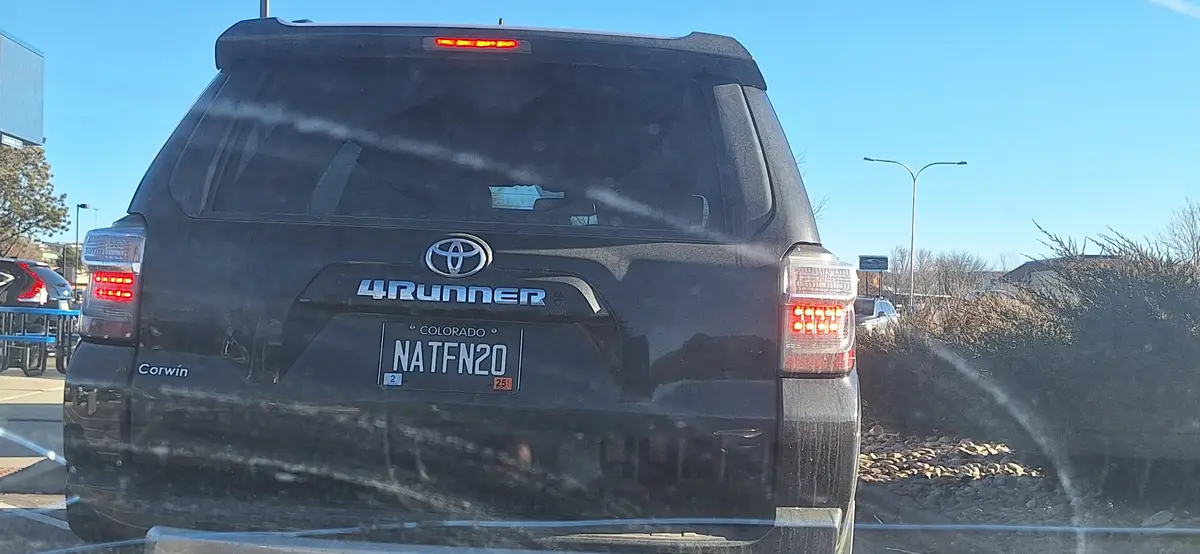 The rear of a black Toyota 4Runner is covered in dirt, parked in a lot under a clear blue sky. The Colorado license plate…