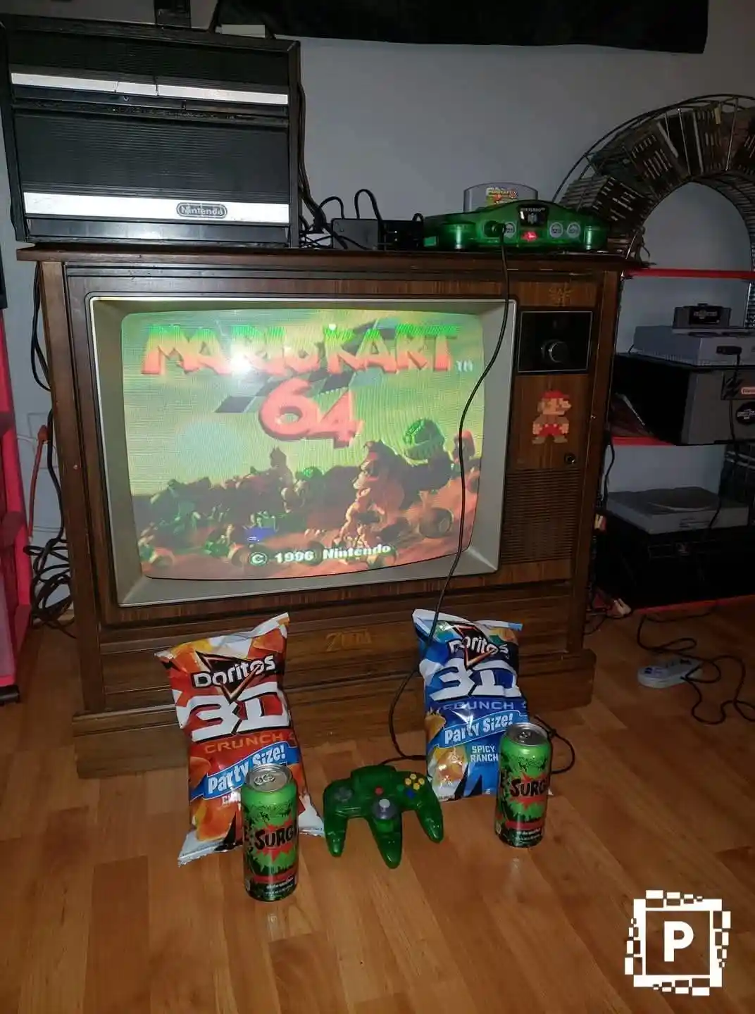 A vintage wooden TV set displays the 'Mario Kart 64' title screen, with a green N64 console and controller on top and on the…
