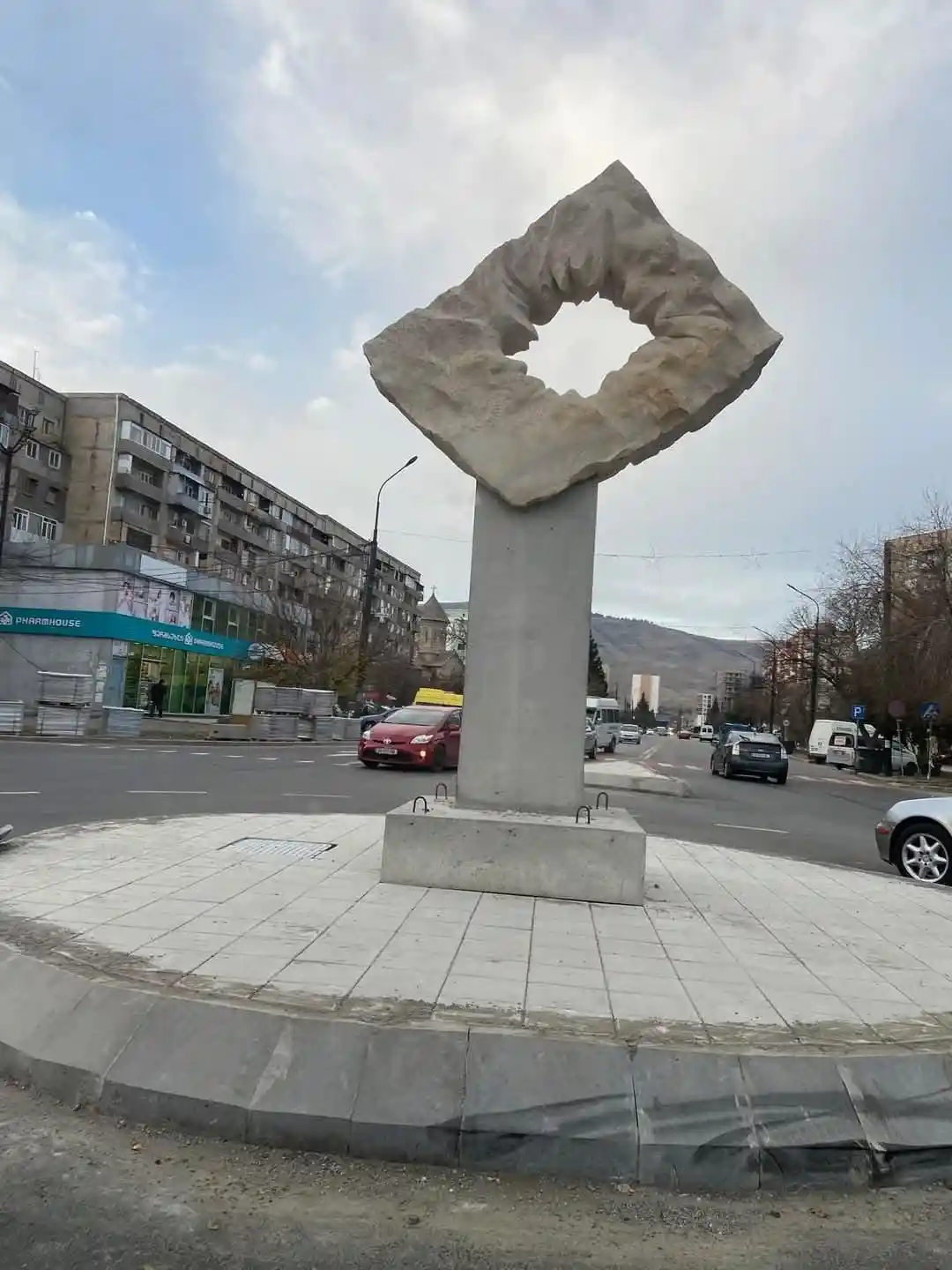 a large, abstract stone sculpture shaped like a giant scrunchie sits atop a concrete pedestal in the middle of a city street…