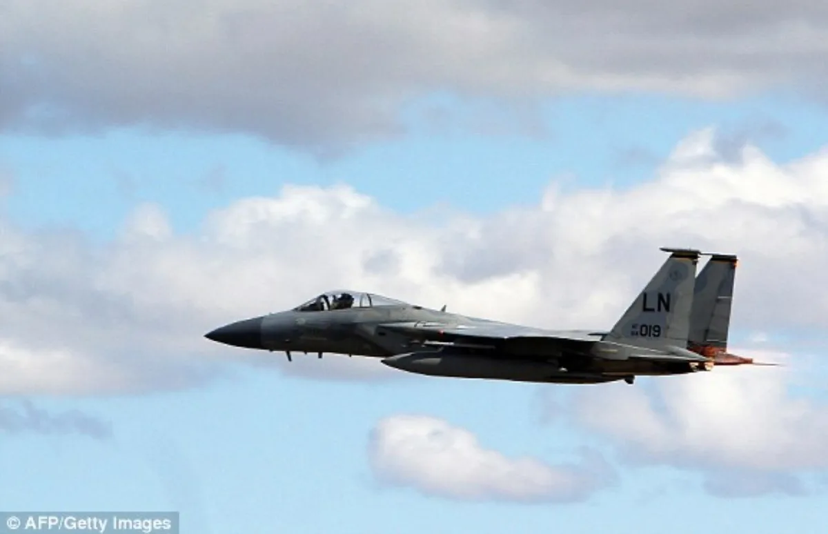 A gray fighter jet, likely an F-15, is shown in flight against a partly cloudy blue sky. The aircraft has 'LN' and '019'…