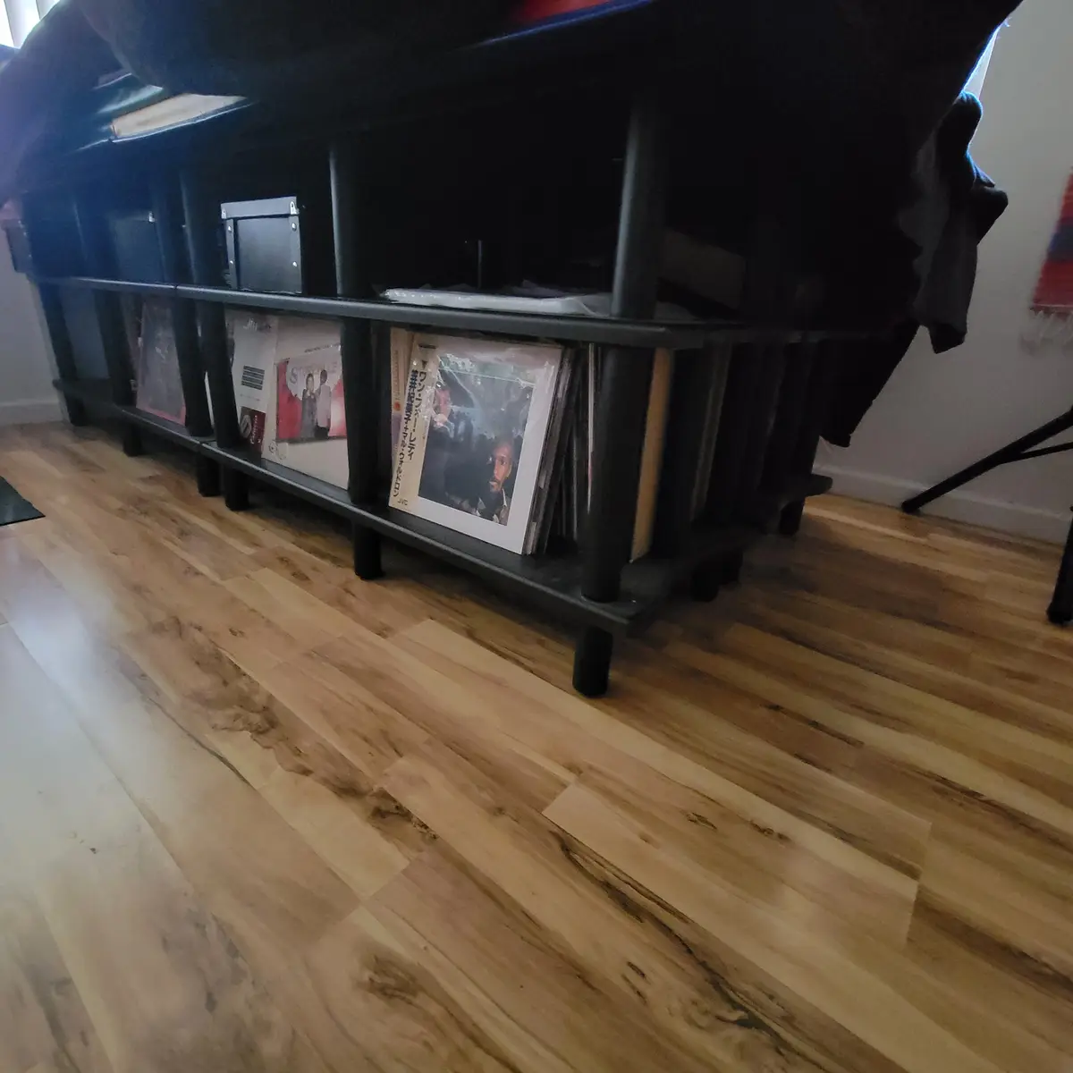 A low-angle shot of a black metal shelving unit holding vinyl records on a light wood floor, with the overlaid text 'i have…