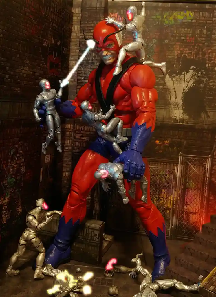 A large red and blue superhero action figure, resembling Daredevil, is surrounded by numerous smaller silver robot action…