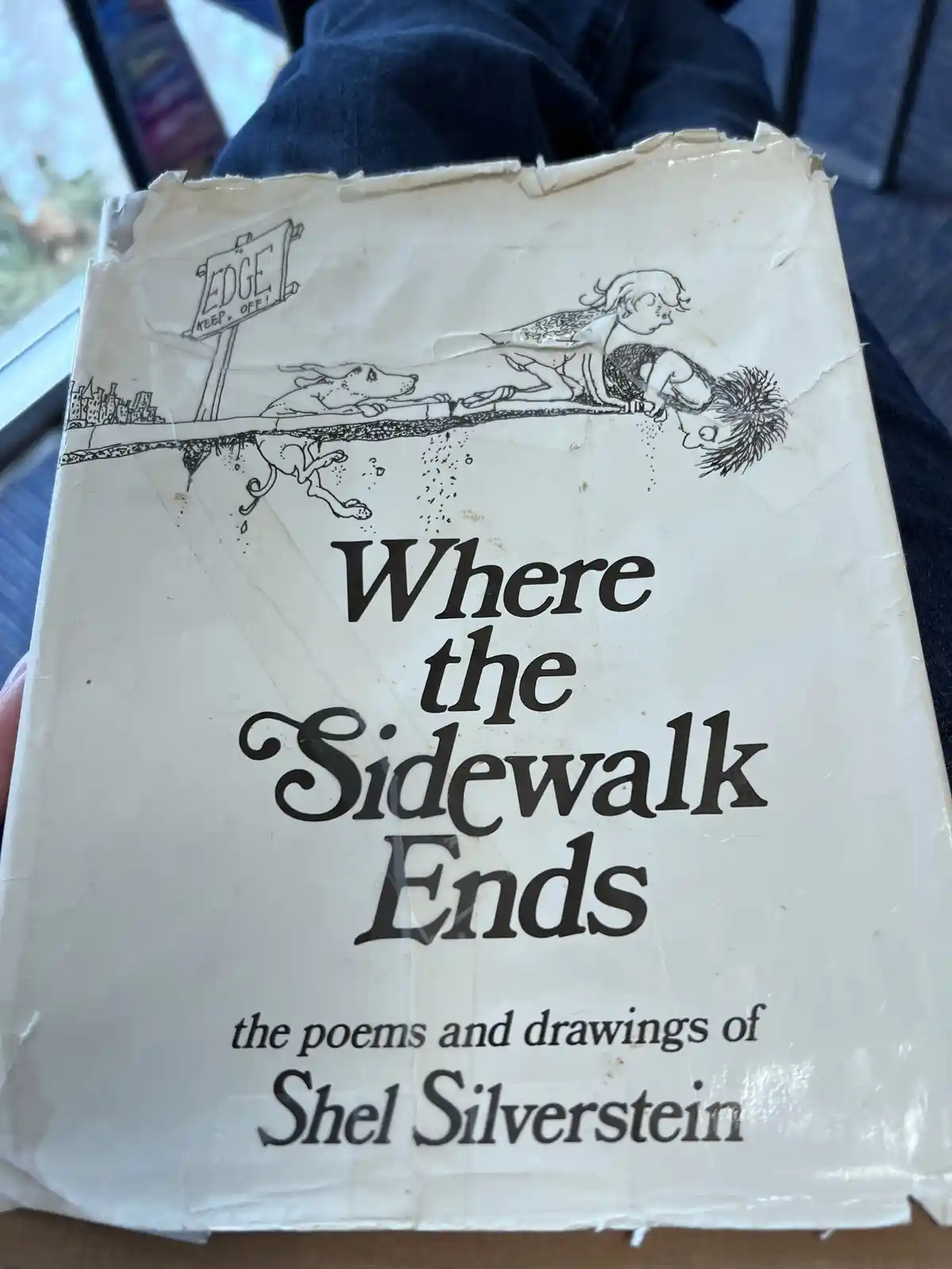 A close-up photo of a well-worn copy of Shel Silverstein's book 'Where the Sidewalk Ends', showing its cover art of a child…