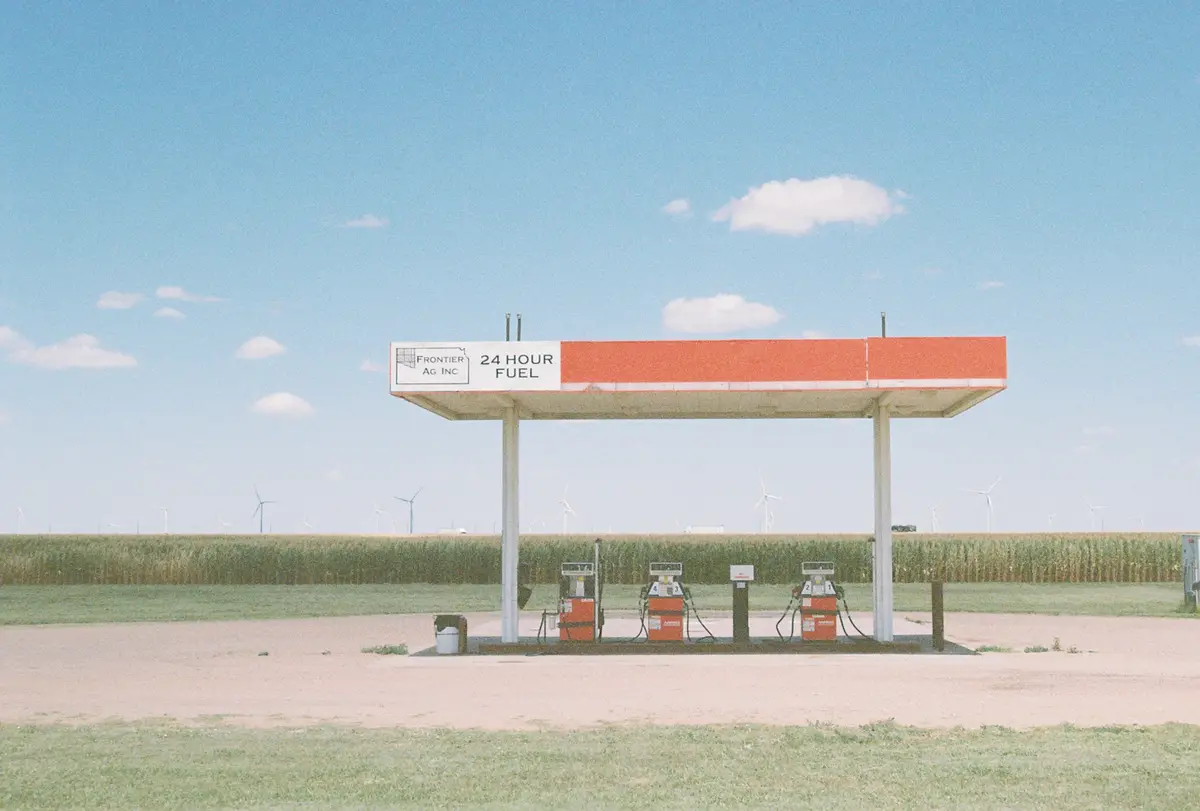 An empty, rustic gas station with a red and white canopy labeled 'FRONTIER AG INC 24 HOUR FUEL' stands in a vast, open field…