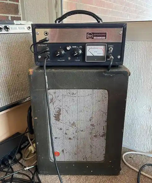 A vintage, worn black guitar amplifier with a 'KRA' logo and 'Kyle's Bad Amplification' text on its front panel sits atop a…