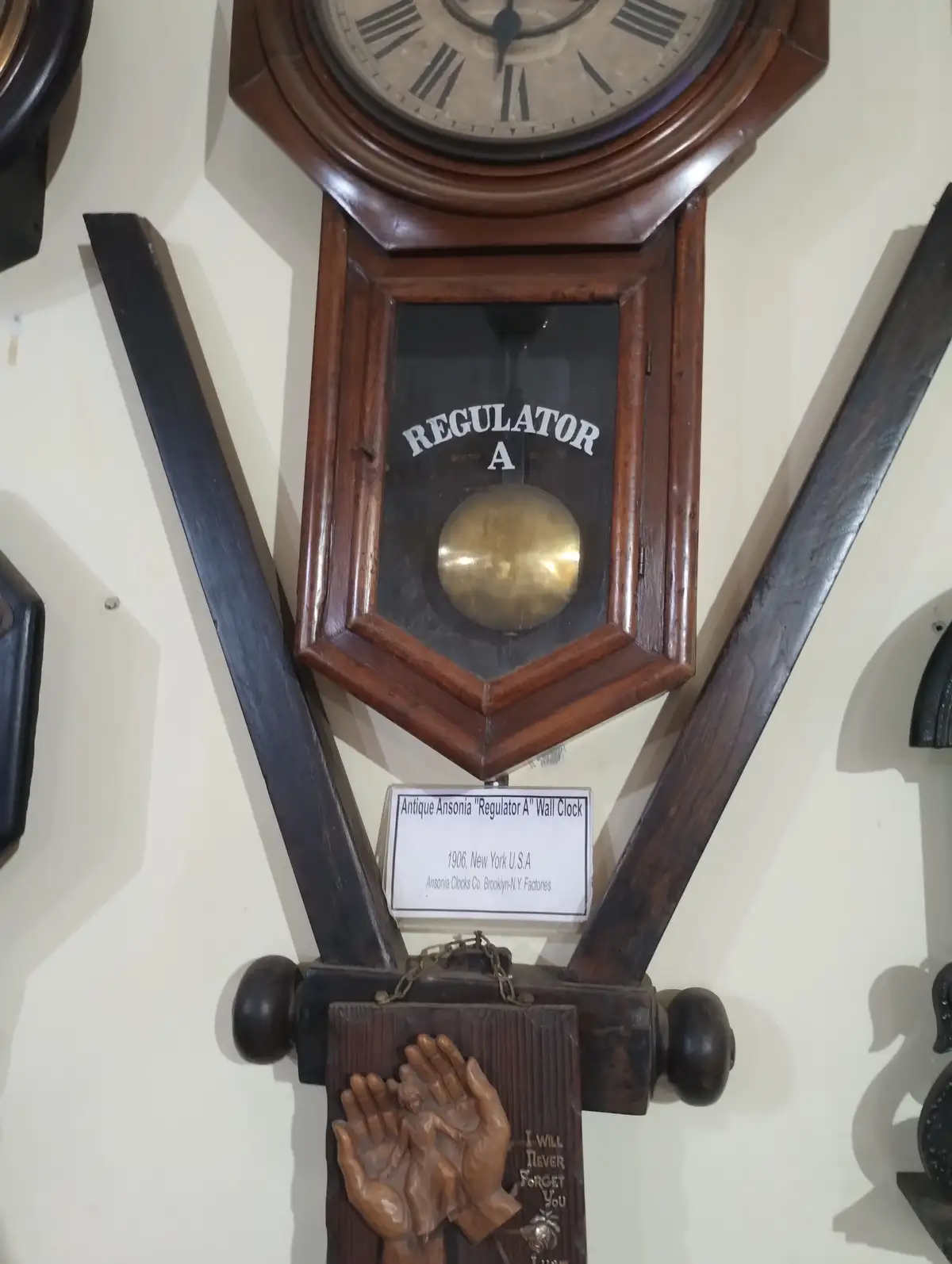 An antique wooden wall clock with a brass pendulum and Roman numerals, labeled 'REGULATOR A', has a carved wooden plaque…