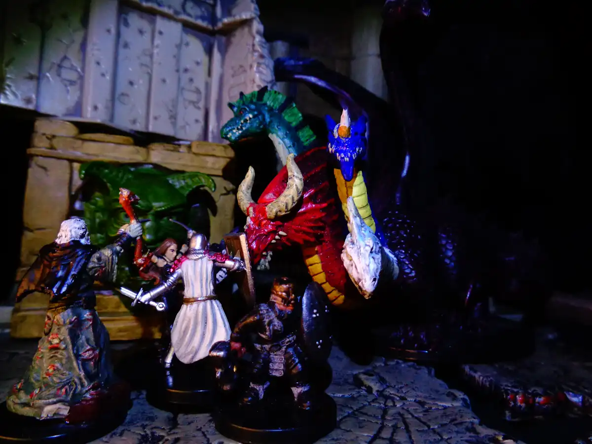 A photo of several painted fantasy miniatures, including three human-like adventurers and three large, colorful dragons…