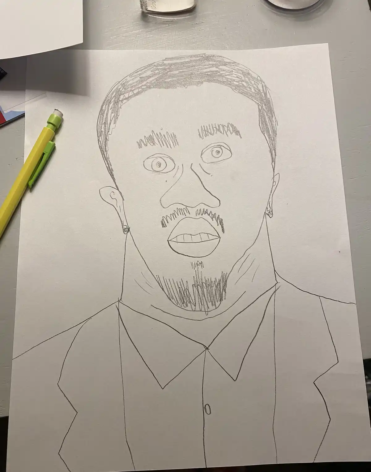 A hand-drawn pencil sketch on white paper depicts a man with wide, startled eyes, a surprised expression, and a goatee…