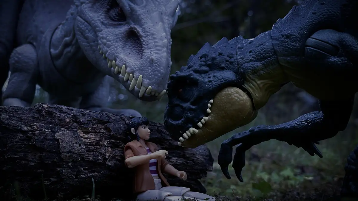 A small human action figure sits calmly between two large, menacing dinosaur action figures, one gray and one black, both…