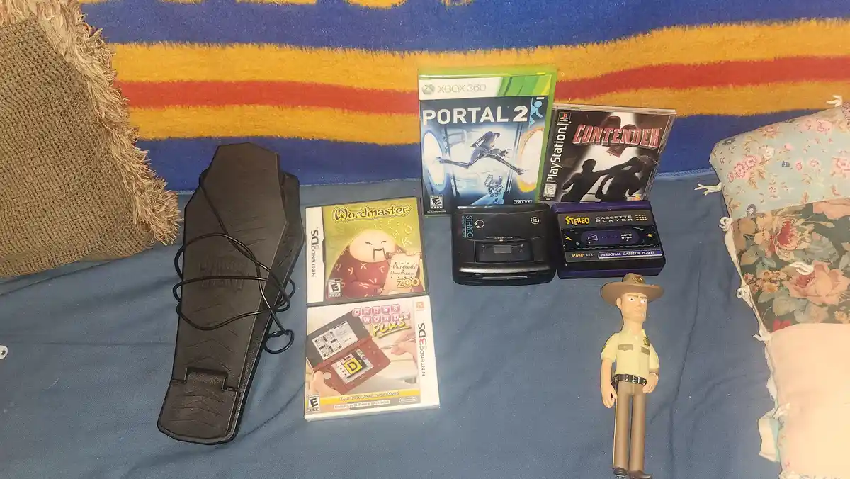 A collection of video game consoles and games, including a Nintendo DS, Xbox 360 Portal 2, PlayStation 1 Contender, and a…