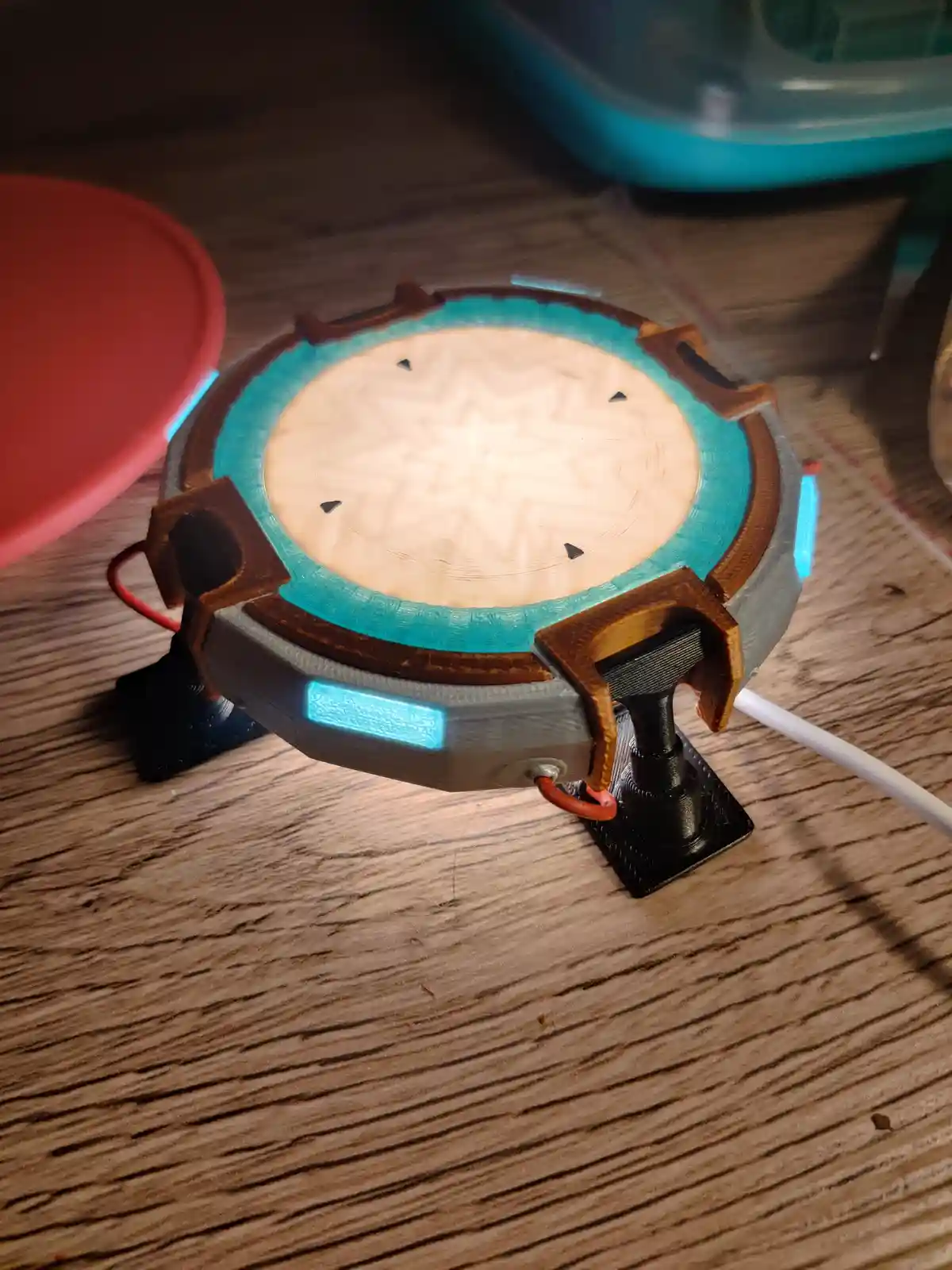 A 3D-printed replica of a Portal gun from the video game Portal sits on a wooden table, featuring glowing blue lights and a…