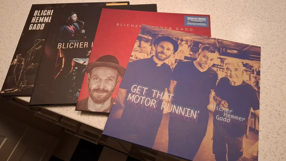 Four vinyl record album covers for the jazz group Blicher Hemmer Gadd are stacked on a speckled countertop. The frontmost…