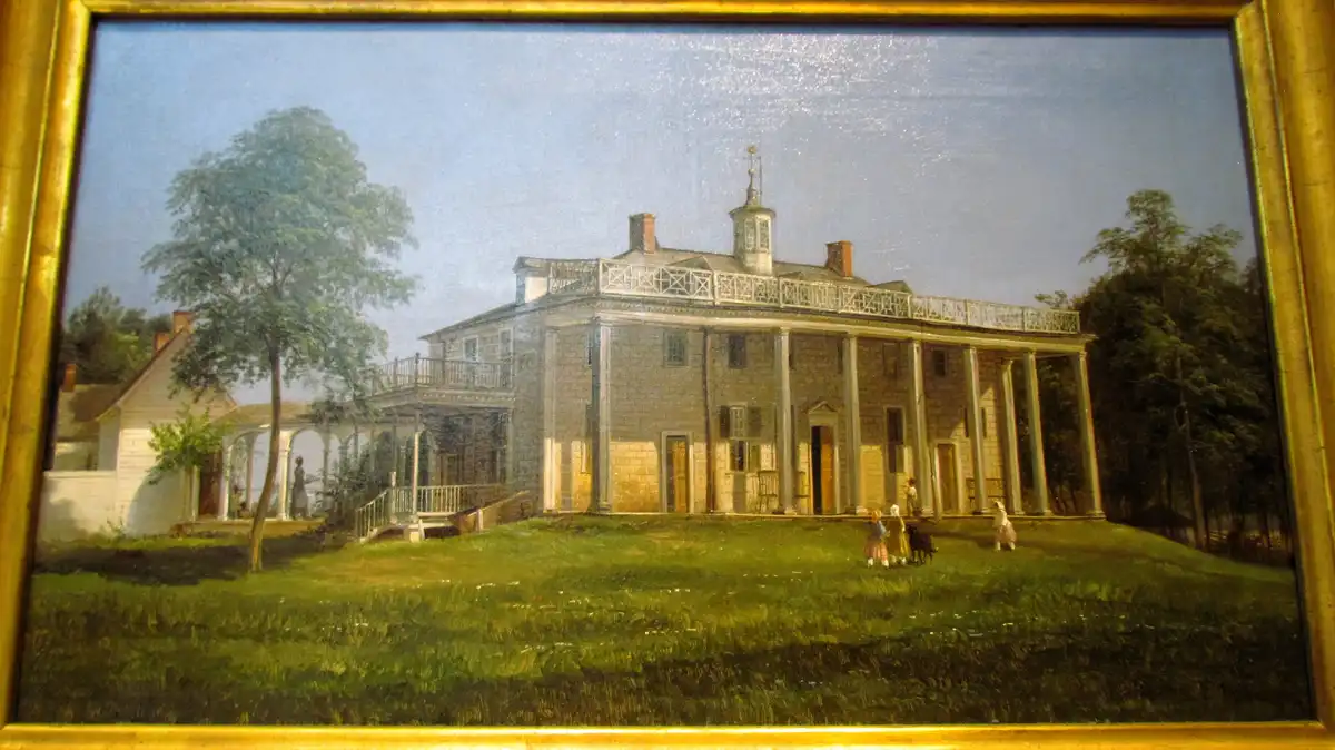 A framed painting depicts a large, classical-style colonial house with columns and balconies, surrounded by green lawn and…