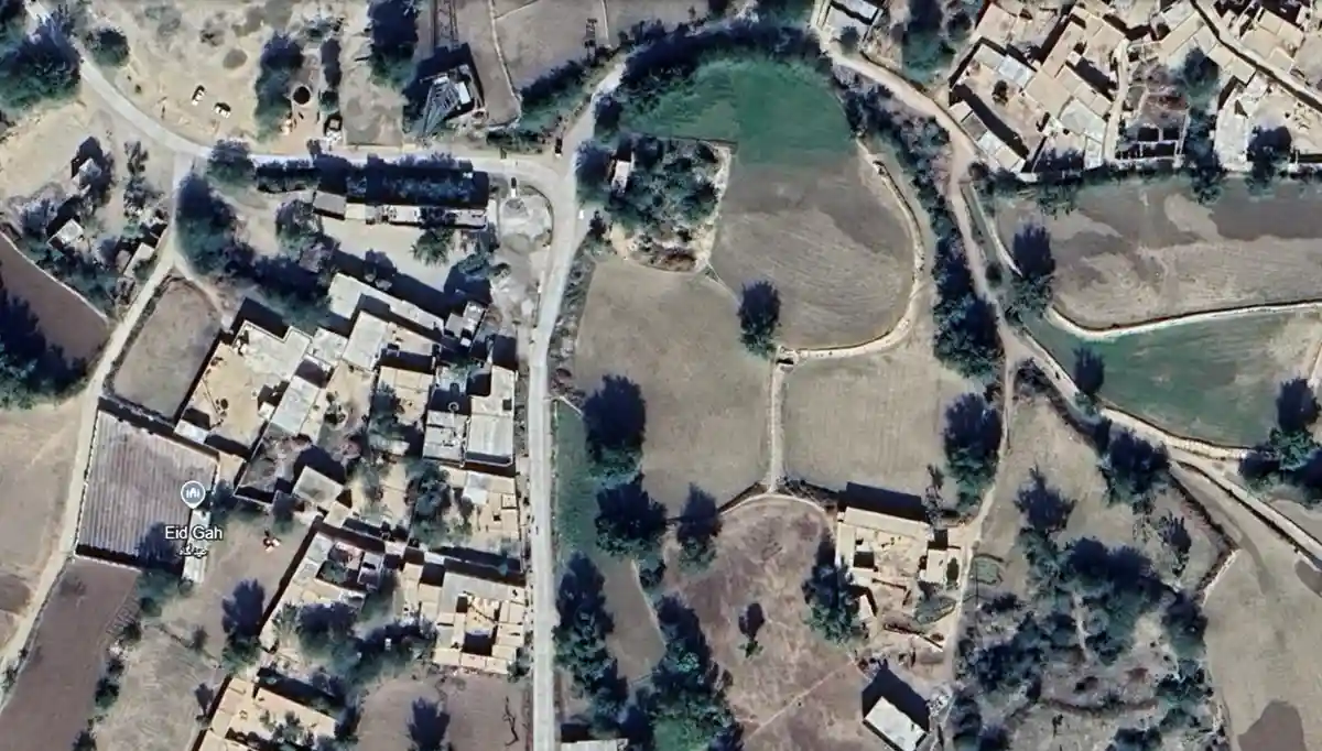 An aerial satellite image shows a rural settlement labeled 'Eid Gah' with surrounding fields and sparse vegetation. The…