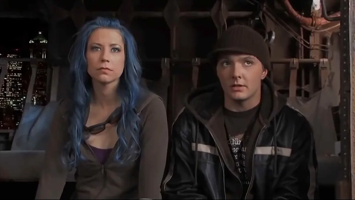 Two characters from the movie 'The Matrix Reloaded' are shown side-by-side; the woman on the left has blue hair and a stern…