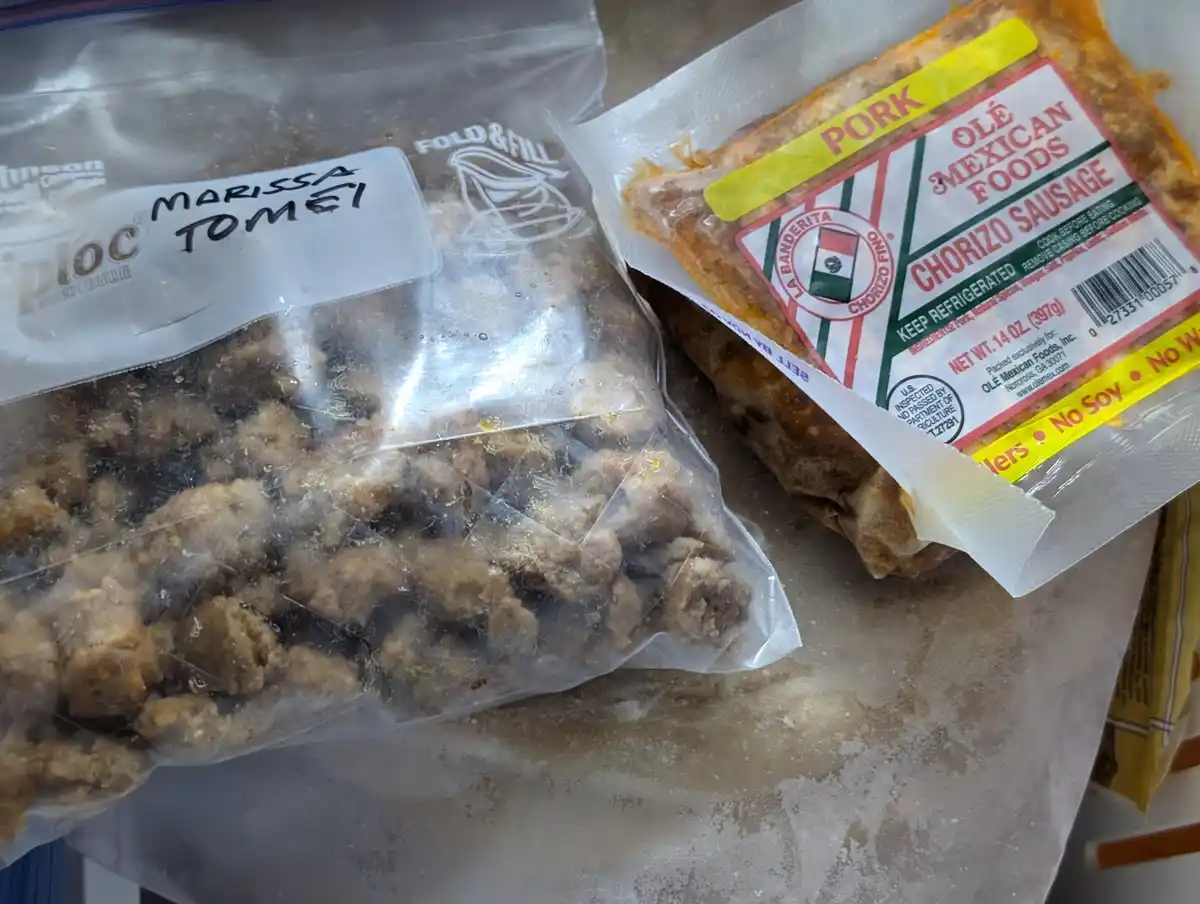 A close-up photo shows two frozen meat packages on a countertop. One is a clear zip-top bag labeled 'MARISSA TOMEI'…